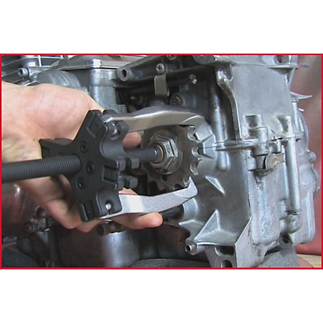 Hand hält Werkzeug zur Demontage von Komponenten eines Motors. Ein Zahnrad wird entfernt.